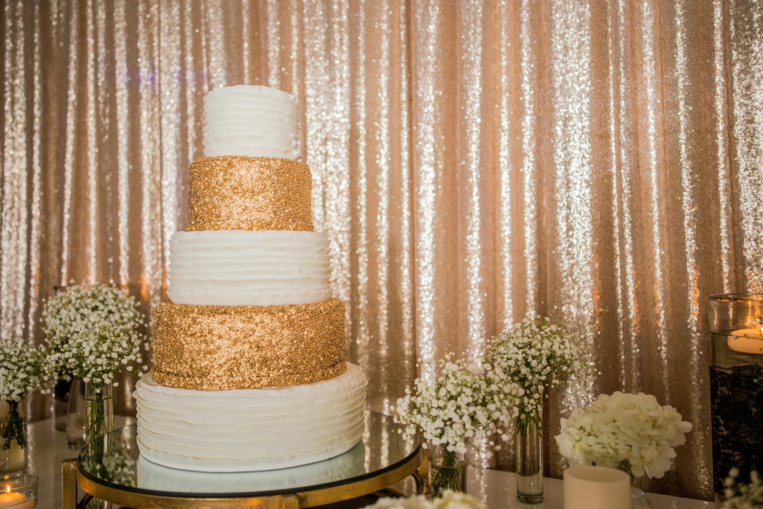 Luxurious four-tier wedding cake adorned with gold sparkle layers and surrounded by baby's breath flowers.